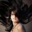 Woman with long black hair flipping it in the air after hair scalp treatment.